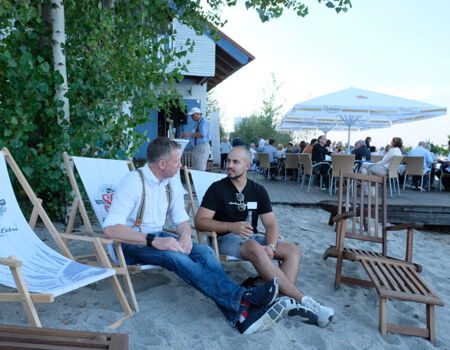 Zwei Menschen sitzen gemütlich am Strand und trinken Bier.